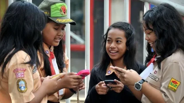 Anak-anak sekolah di Indonesia membuka Facebook di perangkat seluler mereka. Sumber Getty Images