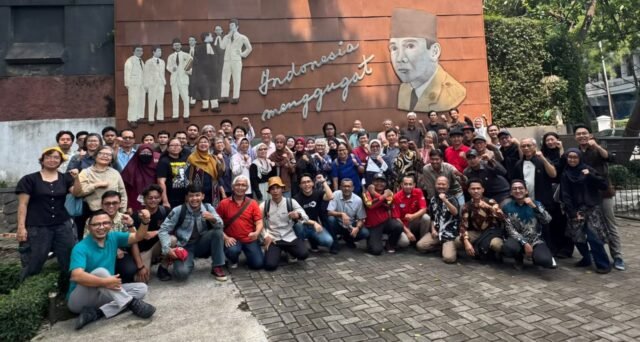 Puluhan peserta pertemuan FIAD berfoto bersama sambil mengepalkan tangan di depan mural Indonesia Menggugat, Bandung
